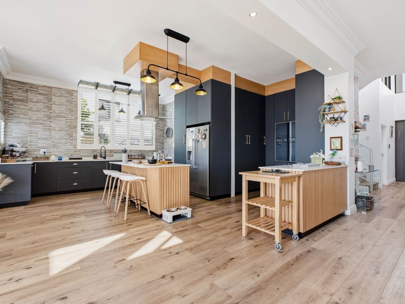 Modern open-plan kitchen featuring dark cabinetry, light wood accents, a central island, integrated appliances, and high-quality laminate flooring.