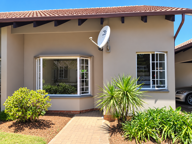 Front elevation of a well-maintained flat featuring a terracotta tiled roof, exposed timber rafters, a bay window, and a paved entrance walkway.
