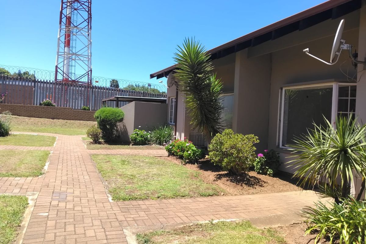 Exterior view of the property featuring a paved walkway, landscaped garden areas, and a secure perimeter fence.