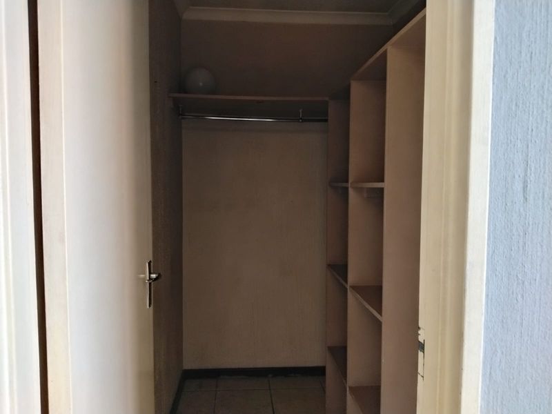 A walk-in closet or dressing area featuring built-in shelving, a hanging rail, and tiled flooring, currently vacant and ready for use.