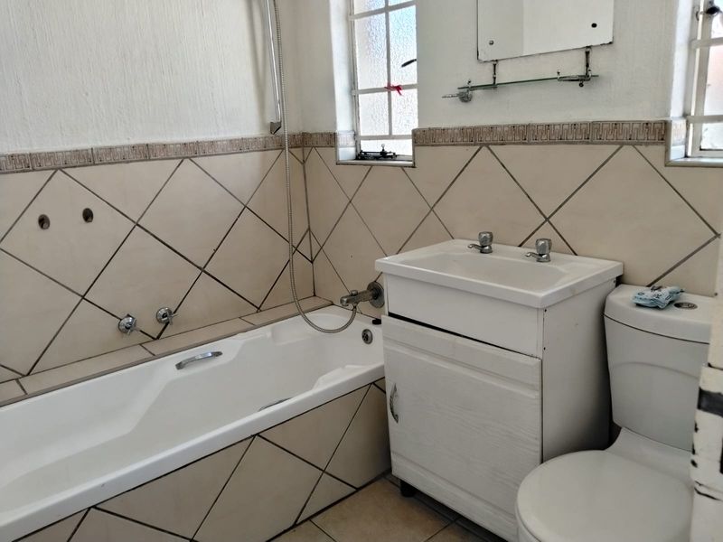A functional bathroom featuring a built-in bathtub, vanity cabinet with basin, and toilet, finished with diamond-patterned wall tiling.