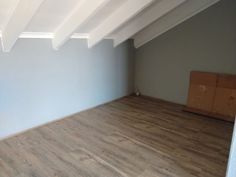 An empty bedroom featuring exposed white rafters, grey walls, and wood-look laminate flooring, offering a clean and versatile space.