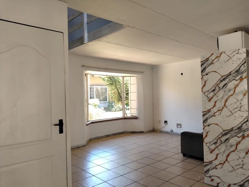 An empty living room featuring tiled flooring, a bay window, and a marble-effect feature pillar, with an adjacent staircase leading to an upper level.