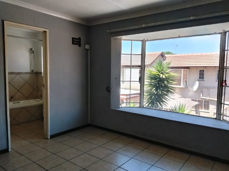 An empty bedroom featuring tiled flooring, a large bay window, and direct access to an en-suite bathroom.