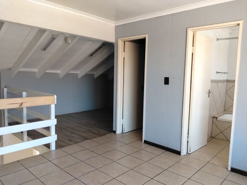 An open-plan loft bedroom area featuring a mix of tiled and laminate flooring, exposed rafters, and direct access to an adjoining bathroom.