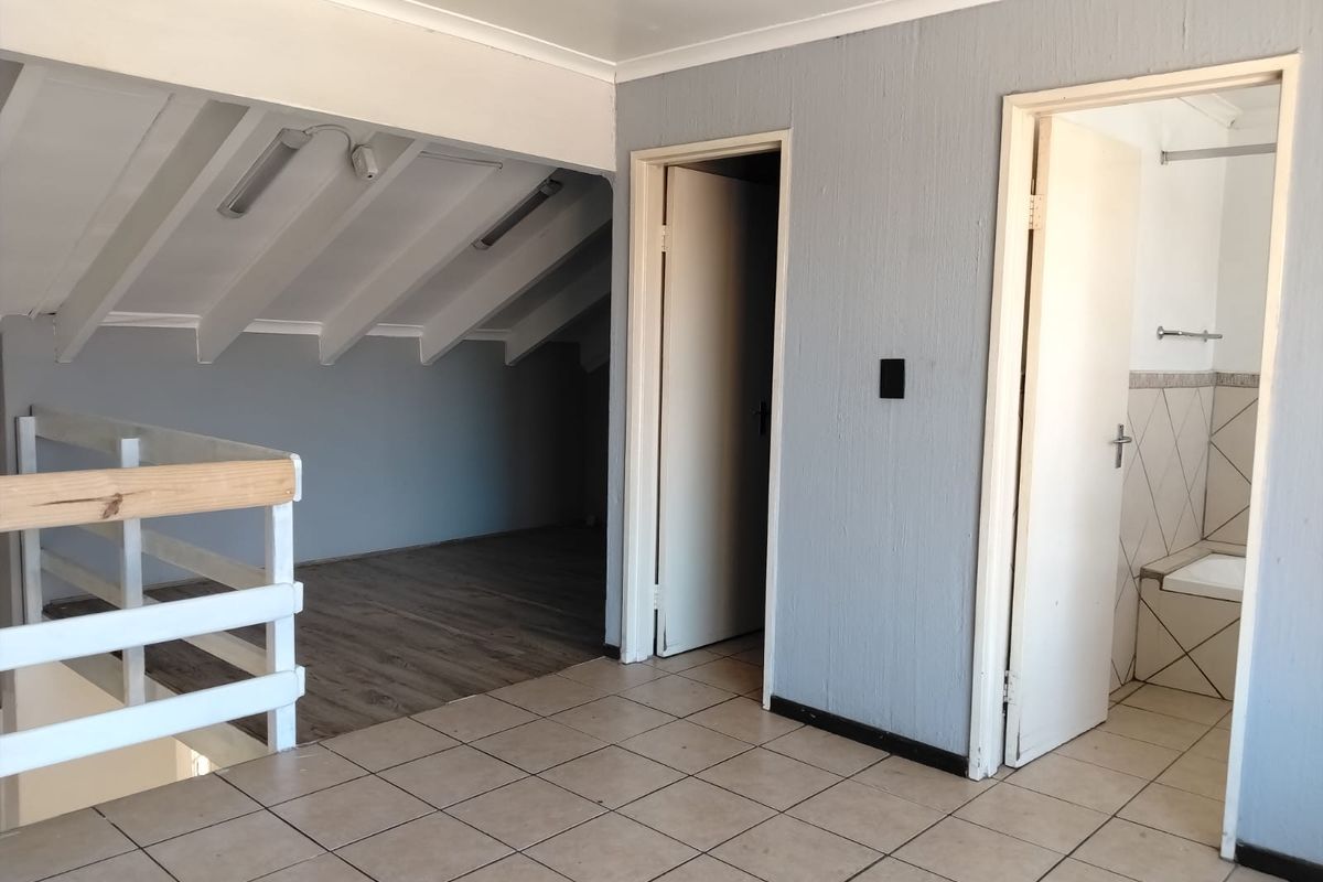 An open-plan loft bedroom area featuring a mix of tiled and laminate flooring, exposed rafters, and direct access to an adjoining bathroom.