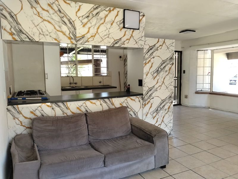 Open plan living and kitchen area featuring marble-effect cabinetry, built-in gas hob, tiled flooring, and a bright bay window.