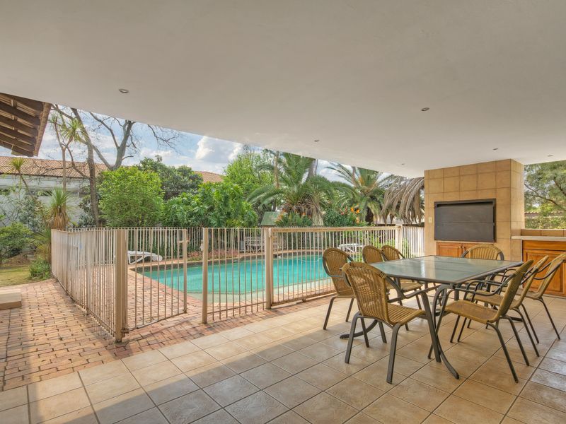 Covered patio area featuring a built-in braai, tiled flooring, and direct access to a fenced swimming pool and garden.