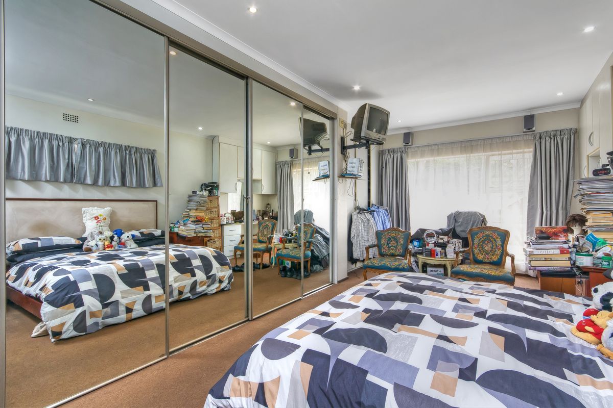 A bedroom featuring wall-to-wall mirrored sliding wardrobes, recessed downlighting, and carpeted flooring, offering ample storage space.