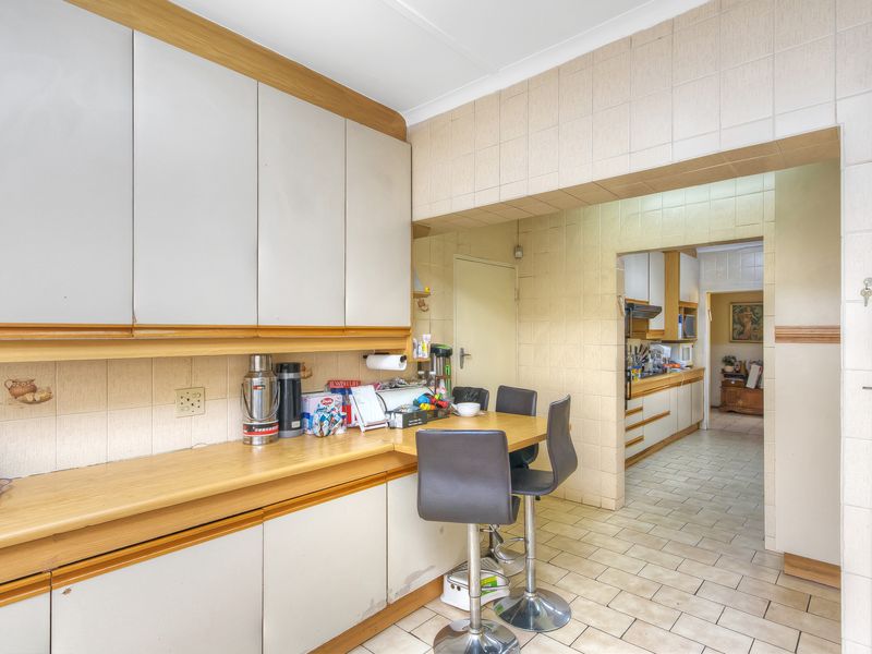 A functional kitchen area featuring extensive built-in cabinetry, laminate countertops, and tiled flooring, with an open-plan layout connecting to an adjacent scullery or prep area.