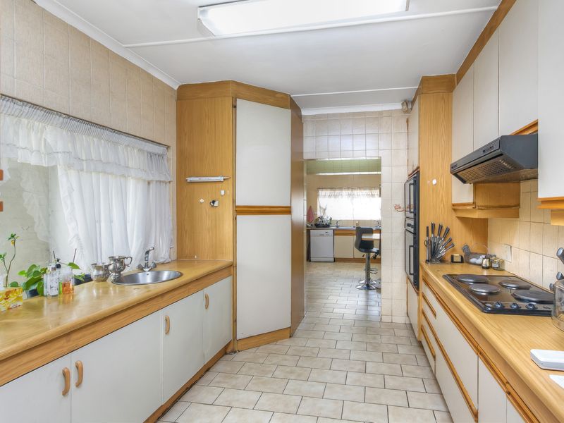 A functional kitchen featuring dated cabinetry, laminate countertops, built-in oven, electric hob, and tiled flooring, with an adjacent scullery area visible.