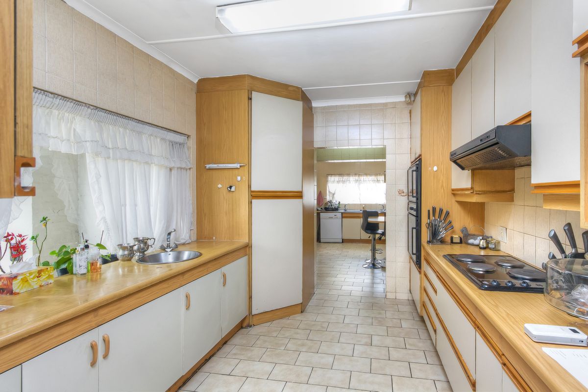 A functional kitchen featuring dated cabinetry, laminate countertops, built-in oven, electric hob, and tiled flooring, with an adjacent scullery area visible.