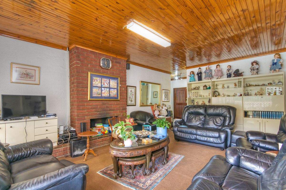 Spacious living room featuring a prominent brick fireplace and traditional timber-paneled ceiling, offering a cozy atmosphere with potential for modern updates.
