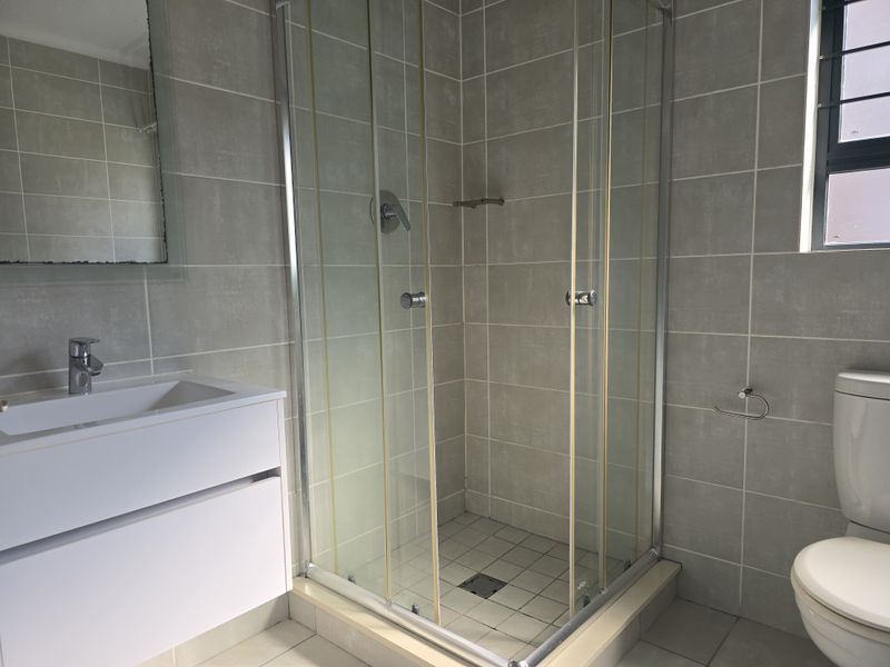A functional bathroom featuring a glass shower enclosure, modern vanity with basin, and tiled finishes throughout.