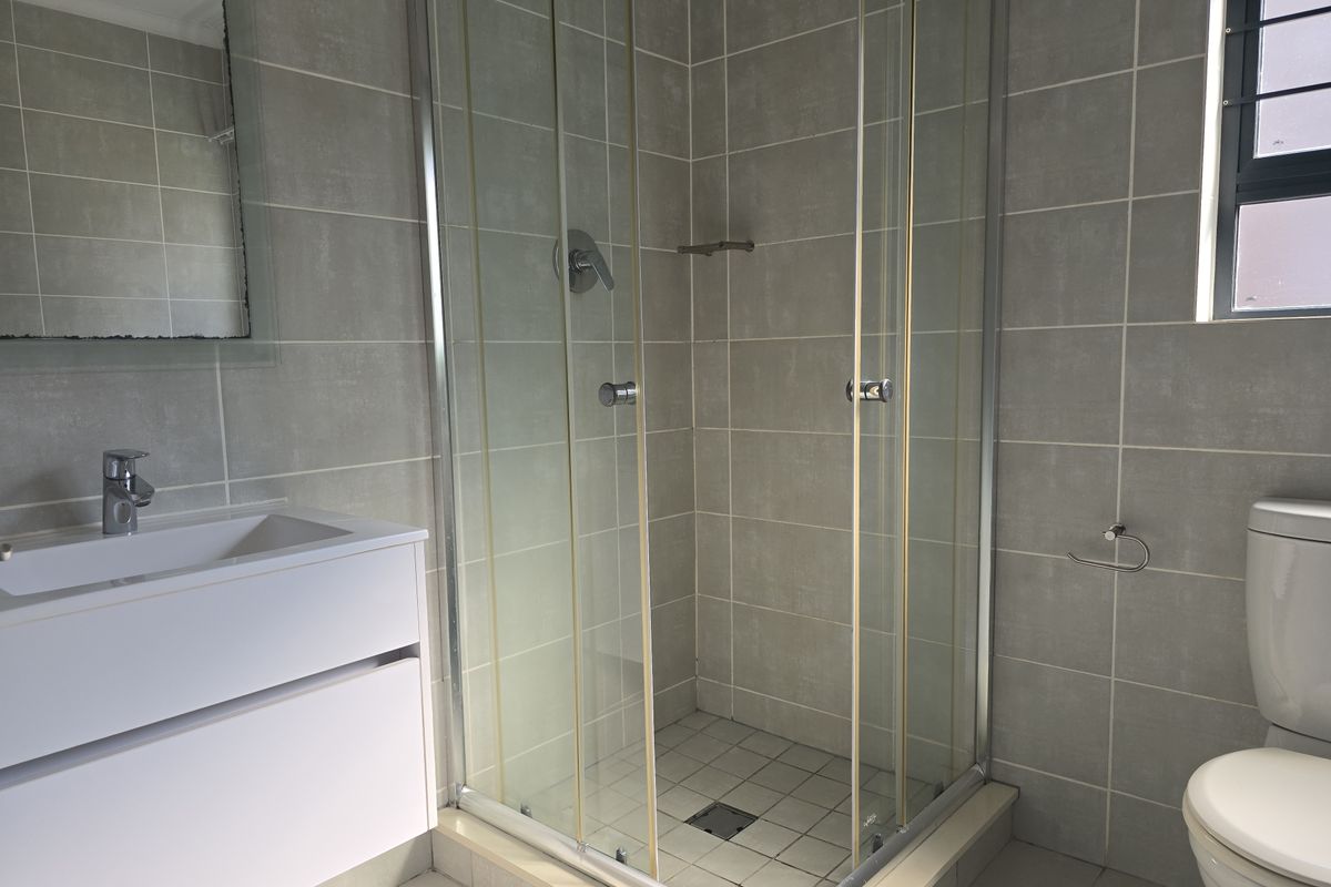 A functional bathroom featuring a glass shower enclosure, modern vanity with basin, and tiled finishes throughout.
