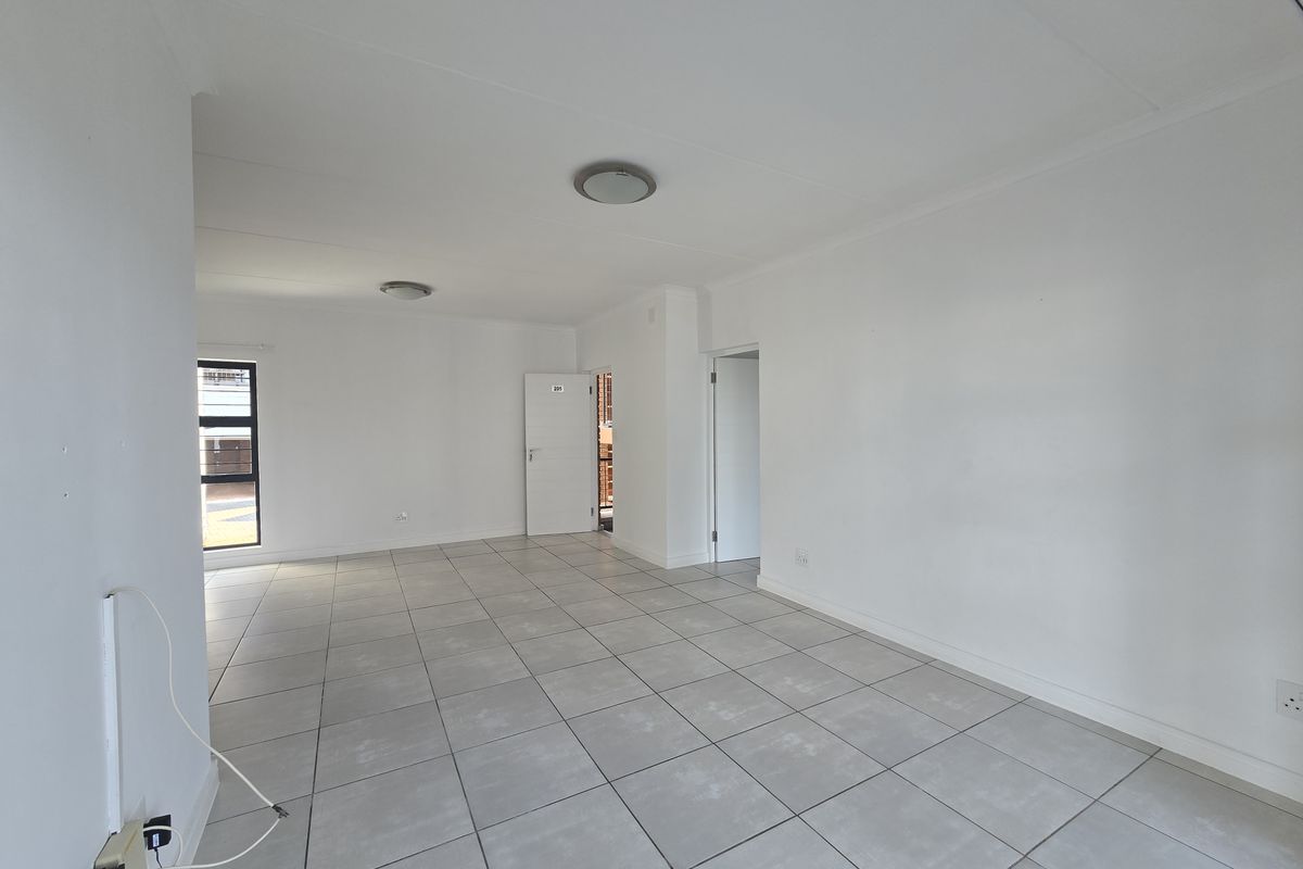 A bright, empty living area featuring neutral tiled flooring, clean white walls, and modern flush mount ceiling lighting.
