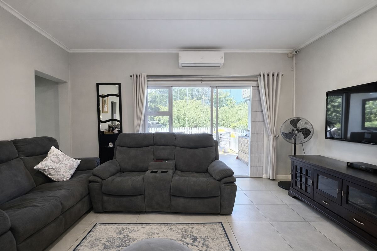 A well-maintained living room featuring tiled flooring, a wall-mounted air conditioning unit, and large sliding glass doors providing access to the outdoor area.