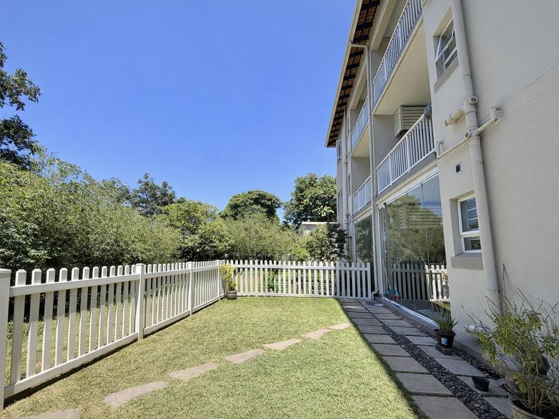 A well-maintained rear garden area featuring a white picket fence, paved walkway, and direct access to the apartment via large glass sliding doors.