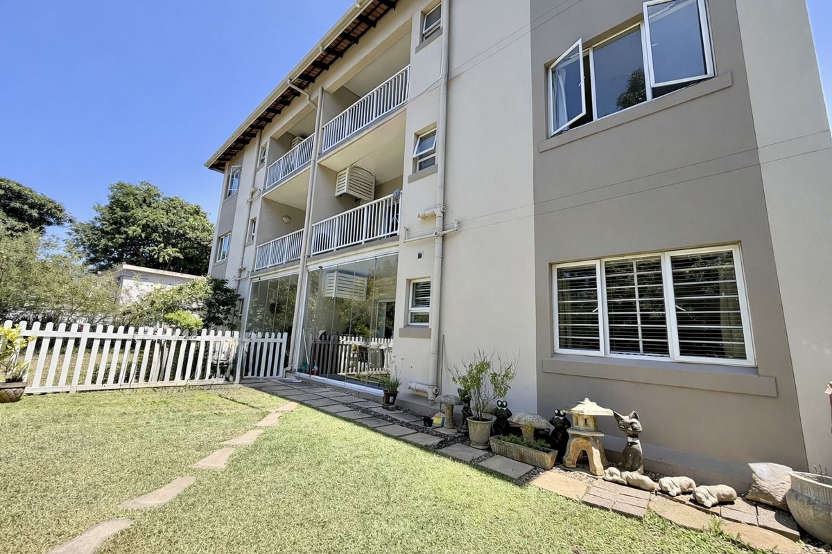 Rear view of a multi-story apartment building featuring private balconies, sliding glass doors, and a well-maintained garden area with a white picket fence.