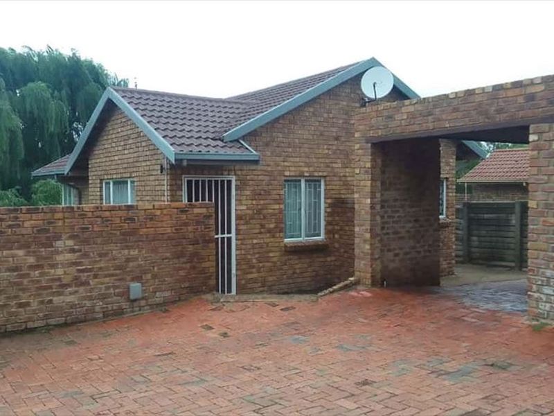 Front exterior view of a face-brick townhouse featuring a paved driveway, attached carport, and a single garage with a roller door.