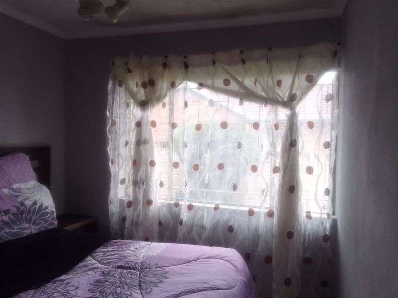 A bedroom featuring a window with security bars and a ceiling light fixture.