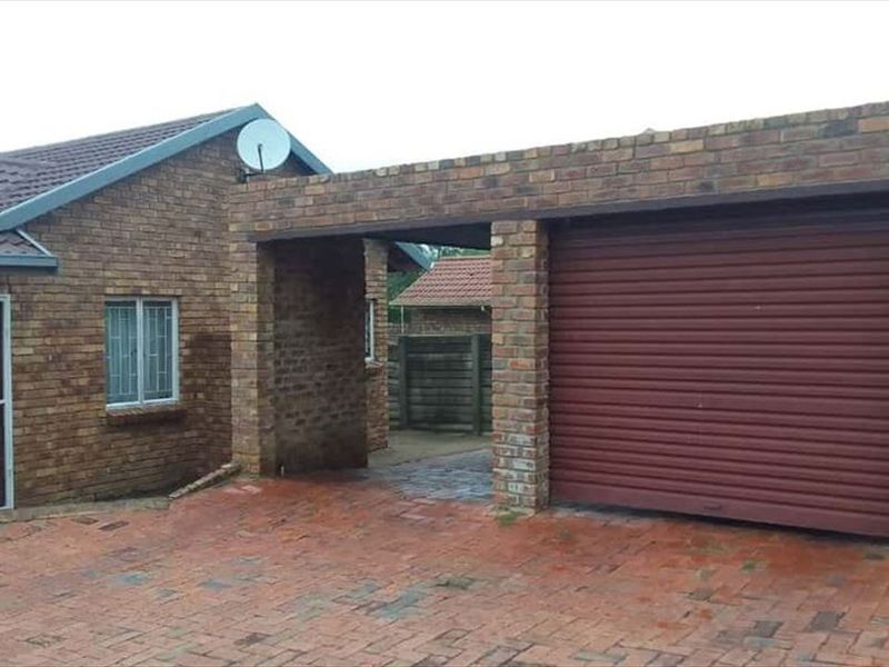 Front exterior view of a face brick townhouse featuring a paved driveway, a secure garage with a roller door, and security-fitted windows.