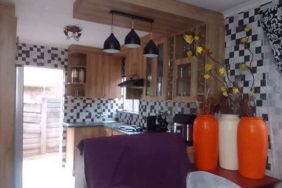 A functional kitchen featuring wood-finish cabinetry, a tiled backsplash, and integrated cooking appliances, with direct access to an outdoor area.