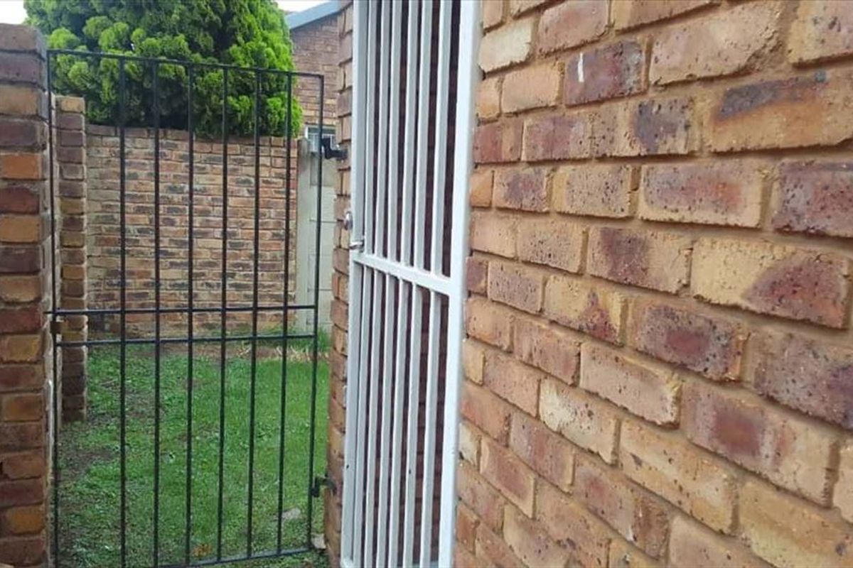 A side access area featuring face brick walls and secure metal gates leading to a small garden space.