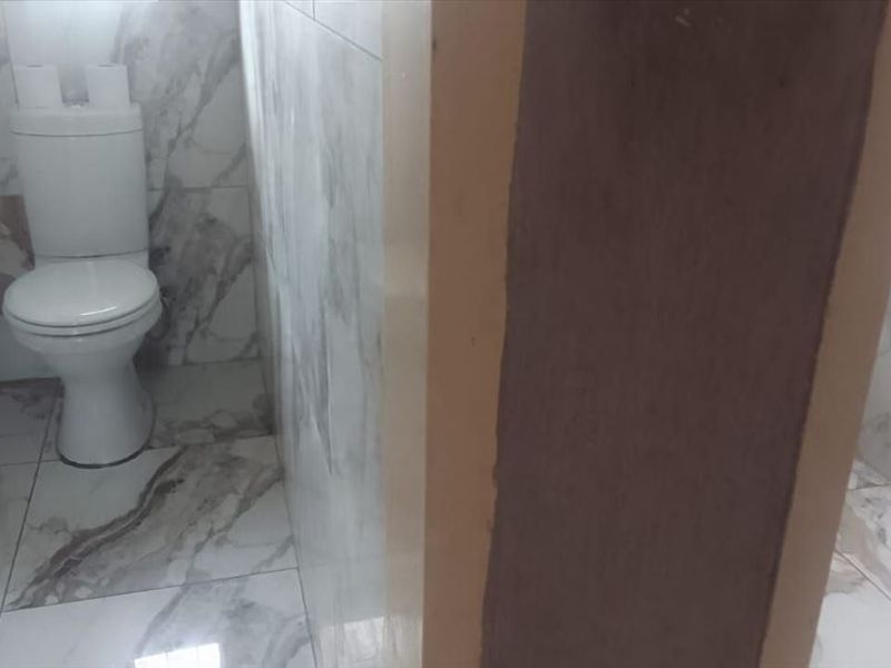A bathroom featuring marble-look wall and floor tiles, equipped with a toilet and bathtub, currently showing unfinished wall trim.