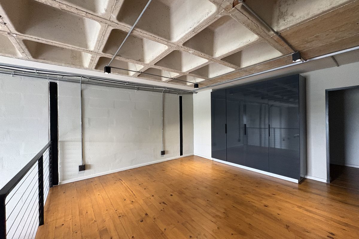 Spacious bedroom featuring industrial-style exposed concrete waffle ceiling, polished timber flooring, and sleek built-in cabinetry with a modern aesthetic.