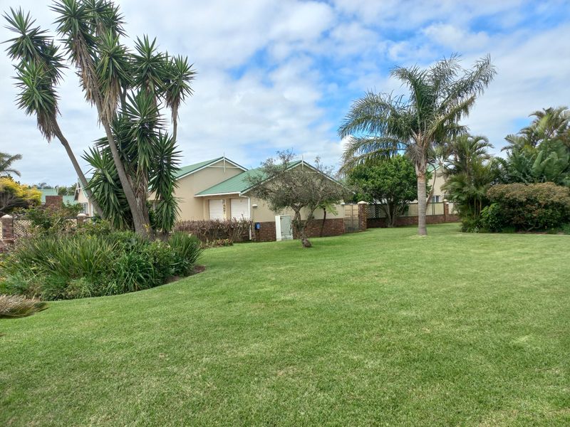 A view of the rear exterior of the townhouse, featuring a well-maintained lawn, mature landscaping, and a brick boundary wall.