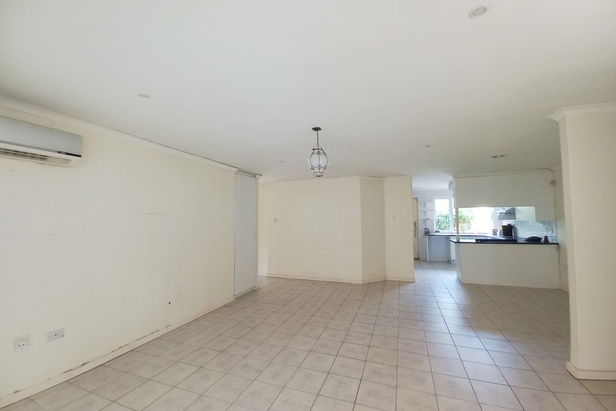 Spacious open-plan living and kitchen area featuring neutral tiled flooring, recessed lighting, and a wall-mounted air conditioning unit.