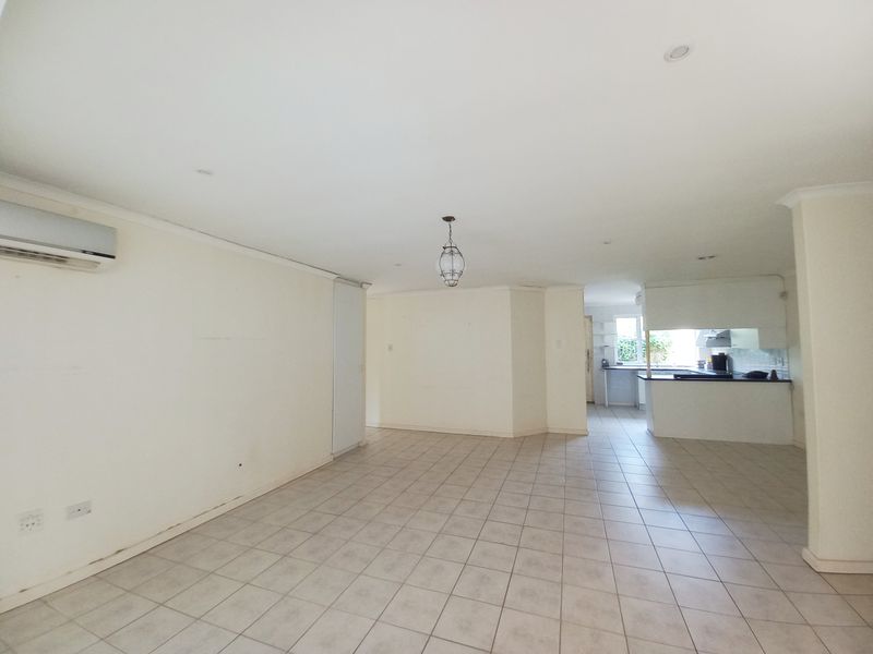 Spacious open-plan living and kitchen area featuring neutral tiled flooring, recessed lighting, and a wall-mounted air conditioning unit.