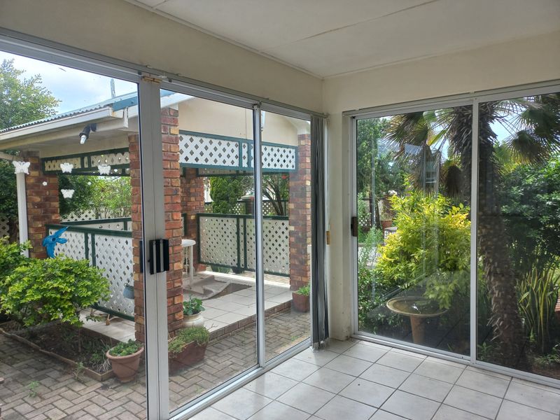 A bright, enclosed patio area featuring large sliding glass doors, tiled flooring, and direct access to an outdoor garden space with brick structural elements.