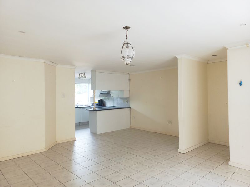 An open-plan living and kitchen area featuring tiled flooring, neutral walls, and a functional kitchen layout with built-in cabinetry and an extractor fan.