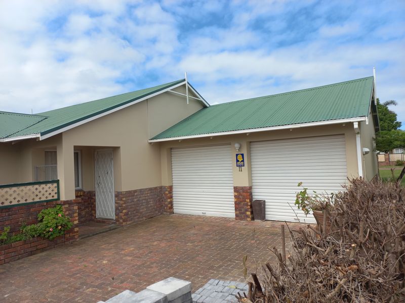 Front elevation of a townhouse featuring a double garage with roller shutter doors, brick paved driveway, and a green corrugated metal roof.