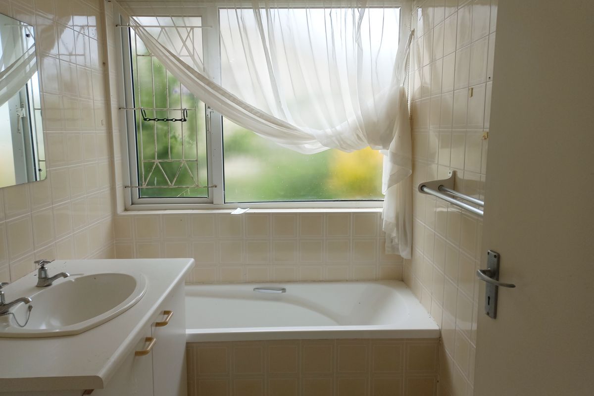 A dated bathroom featuring a built-in vanity, bathtub, and full-height wall tiling, offering potential for a modern renovation.