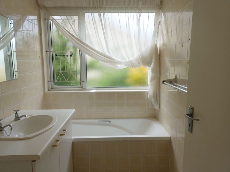 A dated bathroom featuring a built-in vanity, bathtub, and full-height wall tiling, offering potential for a modern renovation.