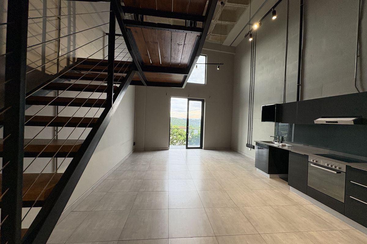 Spacious open-plan living area featuring an industrial-style staircase, modern kitchen with built-in appliances, and large sliding doors leading to an outdoor space.
