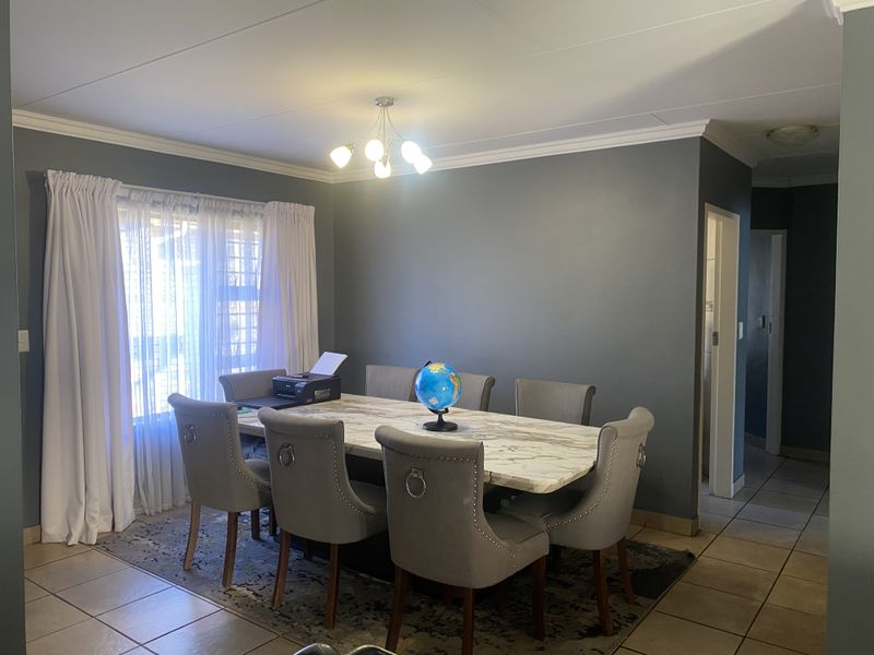 A well-maintained dining room featuring neutral tiled flooring, decorative ceiling cornicing, and a central light fixture, providing a functional space for family meals.