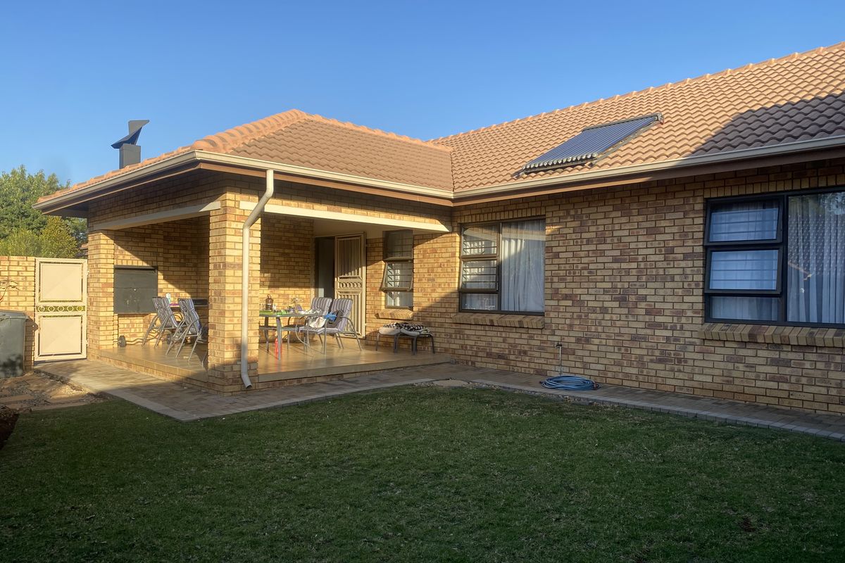 Rear view of a brick townhouse featuring a covered patio with a built-in braai, solar water heating system, and a well-maintained garden area.