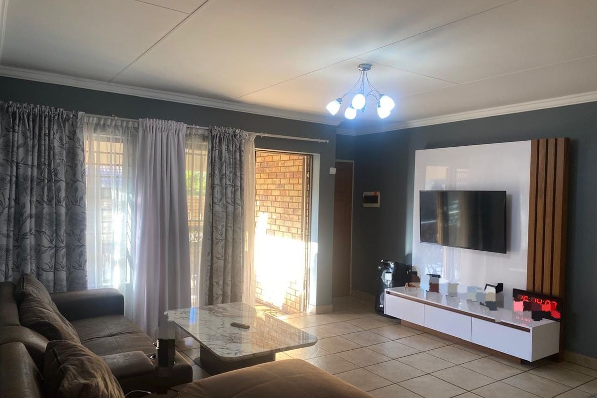 A well-maintained living room featuring tiled flooring, a modern built-in media wall unit, and direct access to an outdoor area through a sliding glass door.