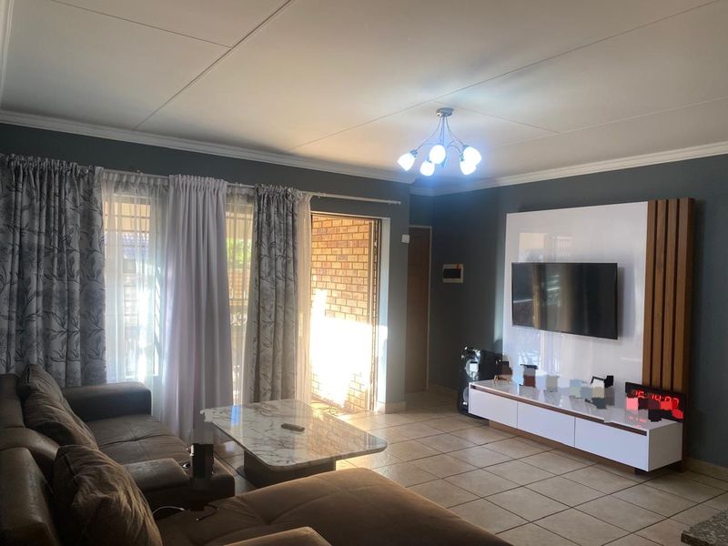 A well-maintained living room featuring tiled flooring, a modern built-in media wall unit, and direct access to an outdoor area through a sliding glass door.