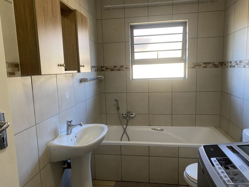 A functional bathroom featuring a pedestal basin, built-in bathtub, wall-mounted cabinetry, and neutral tiled finishes throughout.