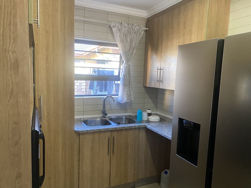 A functional scullery area featuring wood-look laminate cabinetry, a double bowl stainless steel sink, and tiled splashbacks, providing efficient workspace for kitchen preparation.