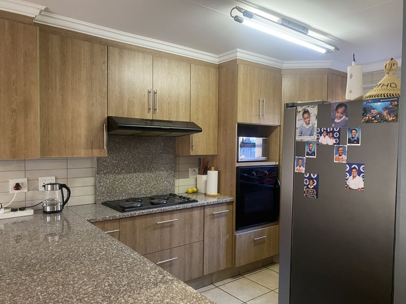 A functional kitchen featuring wood-look laminate cabinetry, granite countertops, a built-in oven, and an electric hob with an extractor fan.