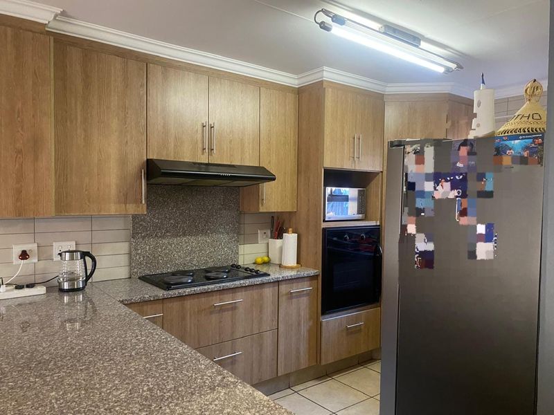 A functional kitchen featuring wood-look cabinetry, granite countertops, built-in oven, electric hob, and tiled flooring with classic coving detail.