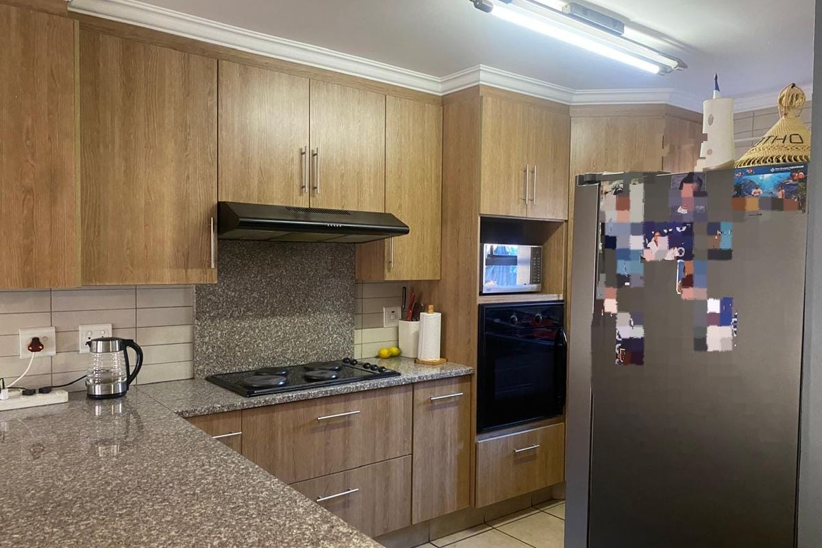A functional kitchen featuring wood-look cabinetry, granite countertops, built-in oven, electric hob, and tiled flooring with classic coving detail.