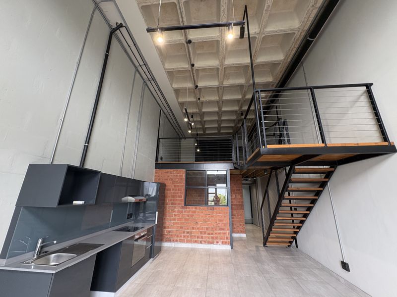 Modern industrial-style open-plan apartment featuring a double-volume space, exposed concrete waffle ceiling, mezzanine level, and a sleek contemporary kitchen.
