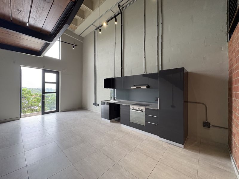 Modern open-plan apartment featuring a sleek kitchen with built-in appliances, high ceilings with exposed industrial elements, and direct access to a private balcony.